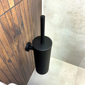 De Mano Black WC-set van yessential.nl is gemonteerd op een wand met houtmotief naast beige tegels, wat zorgt voor een strakke look in de badkamerhoek.