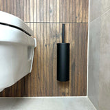 De Cosimo Black WC set van yessential.nl is gemonteerd op een houten wand naast een wit toilet in een moderne badkamer met grijze vloertegels en lichtbeige wandtegels - een elegante badkameraccessoires upgrade.
