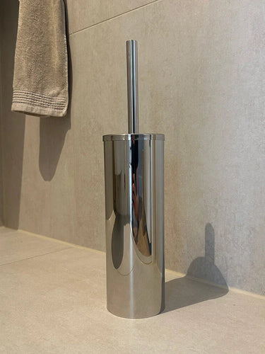 De Tygo Chroom WC Set (no-drill) van yessential.nl heeft een strakke roestvrijstalen toiletborstelhouder met handgreep op een beige tegelvloer, aangevuld met een bijpassende handdoek-alles zonder boren te bevestigen.