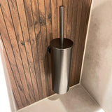 De Sandro Gunmetal WC-set van yessential.nl heeft een moderne roestvrijstalen toiletborstelhouder, aan de muur gemonteerd op houten lambrisering naast lichte tegels - ideaal voor een moderne badkamer.