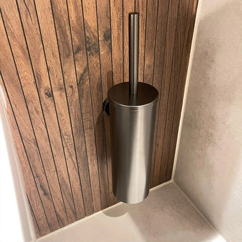 De Sandro Gunmetal WC-set van yessential.nl heeft een moderne roestvrijstalen toiletborstelhouder, aan de muur gemonteerd op houten lambrisering naast lichte tegels - ideaal voor een moderne badkamer.