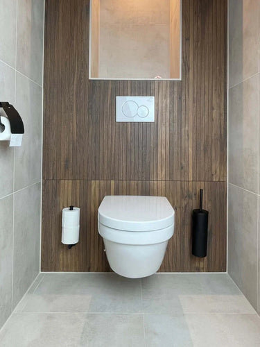 Moderne minimalistische badkamer met wandgemonteerd toilet, wand met houten panelen, ingebouwde toiletpapierhouder links en de Branco Black toiletborstel zwart van yessential.nl rechts. De lichtgrijze tegelvloer en -wanden maken de look compleet.