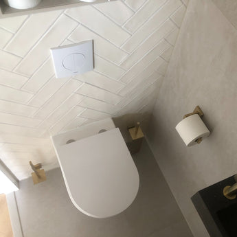 Bovenaanzicht van een moderne badkamer met een wit wandcloset, het Damiano Gold toiletset van yessential.nl en witte wandtegels met chevronpatroon voor een luxe uitstraling.