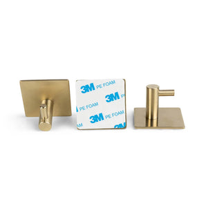 Vier goudkleurige zelfklevende wandhaken uit de 4x Navarro Gold set van yessential.nl worden getoond - twee naar voren gericht, twee naar achteren - met vierkante voet en 3M PE-schuimrug, ideaal als zelfklevende handdoekhaak zonder boren voor eenvoudige installatie.