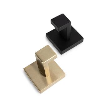 De Valo Gold haak van yessential.nl en een matzwarte vierkante handdoekhaak zijn gerangschikt op een wit oppervlak. Elke RVS haak heeft een geometrisch, hoekig ontwerp met een rechthoekige basis en arm.