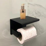 De Tazio Black toiletrolhouder van yessential.nl is bevestigd aan een betegelde muur, met een rol wit toiletpapier met roze hartjes en een pompje zeep of lotion op het planchet.