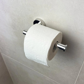 Een rol wit toiletpapier hangt aan de strakke Tino Chroom toiletrolhouder van yessential.nl tegen een licht betegelde badkamermuur en voegt een modern tintje toe aan je badkameraccessoires.