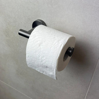 Een rol toiletpapier met een golvend reliëfpatroon hangt aan de Tino Gunmetal toiletrolhouder van yessential.nl, gemonteerd op een lichtgrijze betegelde muur voor een strakke, moderne toevoeging aan je badkameraccessoires.