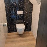 Een moderne badkamer met het yessential.nl Tino Black wandcloset, zwart marmeren achterwand, witte muren, houten vloer, matzwarte accessoires en een RVS toiletrolhouder aan de linkermuur.