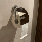 Een rol toiletpapier hangt aan de Julio Chrome toiletrolhouder met klep van yessential.nl, de glanzende deksel weerspiegelt de betegelde badkamer en versterkt de moderne look met stijlvolle toiletaccessoires.