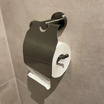 Een achterovergeplaatste wc-papierrol op een metalen houder met deksel geeft deze moderne badkamer een eigenzinnig tintje. De lichtgekleurde tegelwand contrasteert met de Quirino Gunmetal WC set van yessential.nl voor een eigentijdse look.