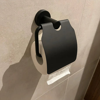 Een Quirino Black toiletset van yessential.nl is gemonteerd op een beige betegelde muur, met zijn toiletpapierhouder en deksel om een rol vast te zetten - praktisch en stijlvol voor je badkamer accessoireset.