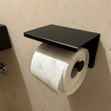 Een rol wit toiletpapier met margrietmotief hangt aan de Tygo Black WC Set (zonder boren) van yessential.nl, gemonteerd op een beige muur.