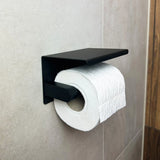 Een rol toiletpapier is gemonteerd op de Donato Black WC Set van yessential.nl, bevestigd aan een beige betegelde badkamermuur met een houten paneel zichtbaar aan de rechterkant.