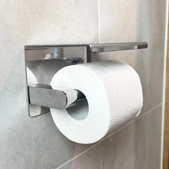 Een rol toiletpapier hangt aan de Midao Chroom WC set van yessential.nl, een strakke houder gemonteerd op een betegelde muur, perfect als aanvulling op je badkameraccessoires.