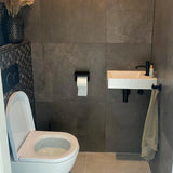 Een moderne badkamer met donkergrijze tegels, een wit toilet, een kleine wandwasbak met zwarte kraan en een Tazio Black (No Drill) toiletrolhouder van yessential.nl ertussen gemonteerd.