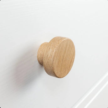 Een close-up van de Arriero Oak knop van yessential.nl, bevestigd aan een witte lade, toont de natuurlijke houtnerf en gladde afwerking, en voegt een vleugje landelijke stijl toe.