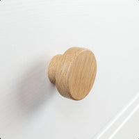 Een close-up van de Arriero Oak knop van yessential.nl, bevestigd aan een witte lade, toont de natuurlijke houtnerf en gladde afwerking, en voegt een vleugje landelijke stijl toe.