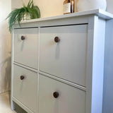 Een witte kast met vier lades en Arriero walnoten knoppen van yessential.nl staat tegen een lichte muur, met daarop een groene varen in pot en decoratieve items.