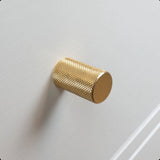 Een close-up van de Remo Gold Deluxe knop een structuur messing cilinder, gemonteerd op een wit kast- of ladefront.