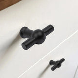Close-up van de Rando Black Knob van yessential.nl in T-vorm met matzwarte afwerking op een witte lade, met een identieke knop op de lade eronder.