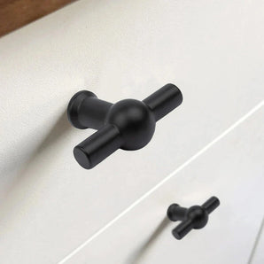 Close-up van de Rando Black Knob van yessential.nl in T-vorm met matzwarte afwerking op een witte lade, met een identieke knop op de lade eronder.