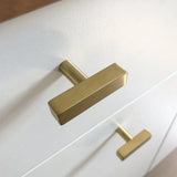 Een close-up van twee moderne Vasco Gold Knobs van yessential.nl, met een luxe gouden afwerking en geborstelde afwerking, verticaal gemonteerd op een wit ladefront.