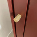 Een close-up van de Remo Gold Deluxe knop van yessential.nl, een luxe meubelknop goud met een gestructureerd cilindrisch ontwerp, getoond op een mat donkerrode kast of lade.