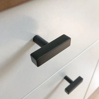 Close-up van twee Vasco Black Knobs van yessential.nl met een matte afwerking op een witte kast. Het moderne, eenvoudige ontwerp heeft strakke lijnen en een stijlvolle uitstraling.