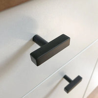 Close-up van twee Vasco Black Knobs van yessential.nl met een matte afwerking op een witte kast. Het moderne, eenvoudige ontwerp heeft strakke lijnen en een stijlvolle uitstraling.