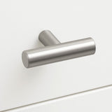 Een Remo RVS knop van yessential.nl, met een geborsteld metalen T-vorm en mat cilindrisch ontwerp, is gemonteerd op een witte kastlade voor een eenvoudige, moderne look.