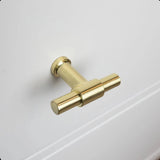 De 10x Cordero Gold Knop van yessential.nl, ideaal voor keukenkastjes knoppen, wordt getoond geïnstalleerd op een witte kastdeur met subtiele paneeldetaillering.