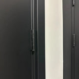 Close-up van twee Ludo Black 76x76 scharnieren van yessential.nl gemonteerd op donkere deuren, met een witte muur ertussen.