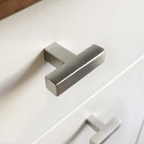 Een close-up van een moderne Vigio RVS knop van yessential.nl op een witte lade, met een andere soortgelijke knop zichtbaar op de lade eronder.