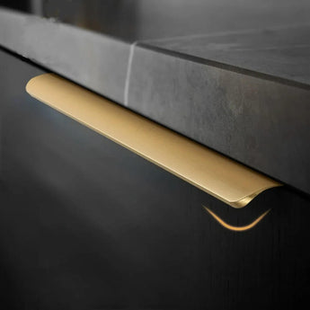 Een close-up van een moderne keukenlade toont het yessential.nl Enzo Gold Deluxe hoekgrepen goud handvat, tegen een donkere kast en een bijpassend aanrechtblad.
