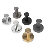 Zes Kyano RVS haken van yessential.nl worden weergegeven op een witte achtergrond in zilver, chroom, goud, matzwart, brons en geborsteld staal. Elke haak heeft een cilindrische pin en een ronde basis.