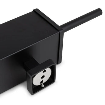 Een close-up van de Alessino Black stekkerdoos van yessential.nl, met een Europees stopcontact en zwart snoer, geplaatst naast een matzwarte toiletborstel voor een strakke, moderne badkamerstijl.
