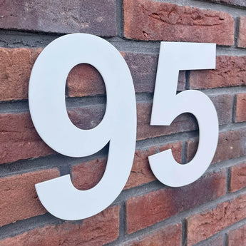 De Adamo White 20cm huisnummer 95 van yessential.nl steekt mooi af tegen een rode bakstenen muur, waardoor gebouw- of huisnummers goed zichtbaar zijn.