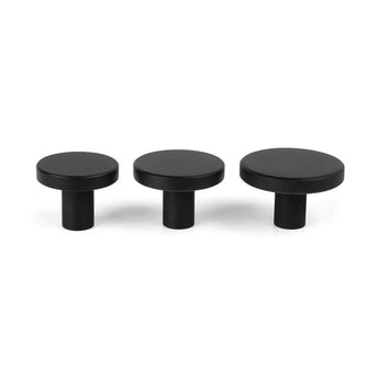 Drie Marizo Black meubelknopjes van yessential.nl in verschillende maten staan op een witte achtergrond en tonen een minimalistisch ontwerp met platte bovenkanten, cilindrische onderkanten en een matte afwerking.
